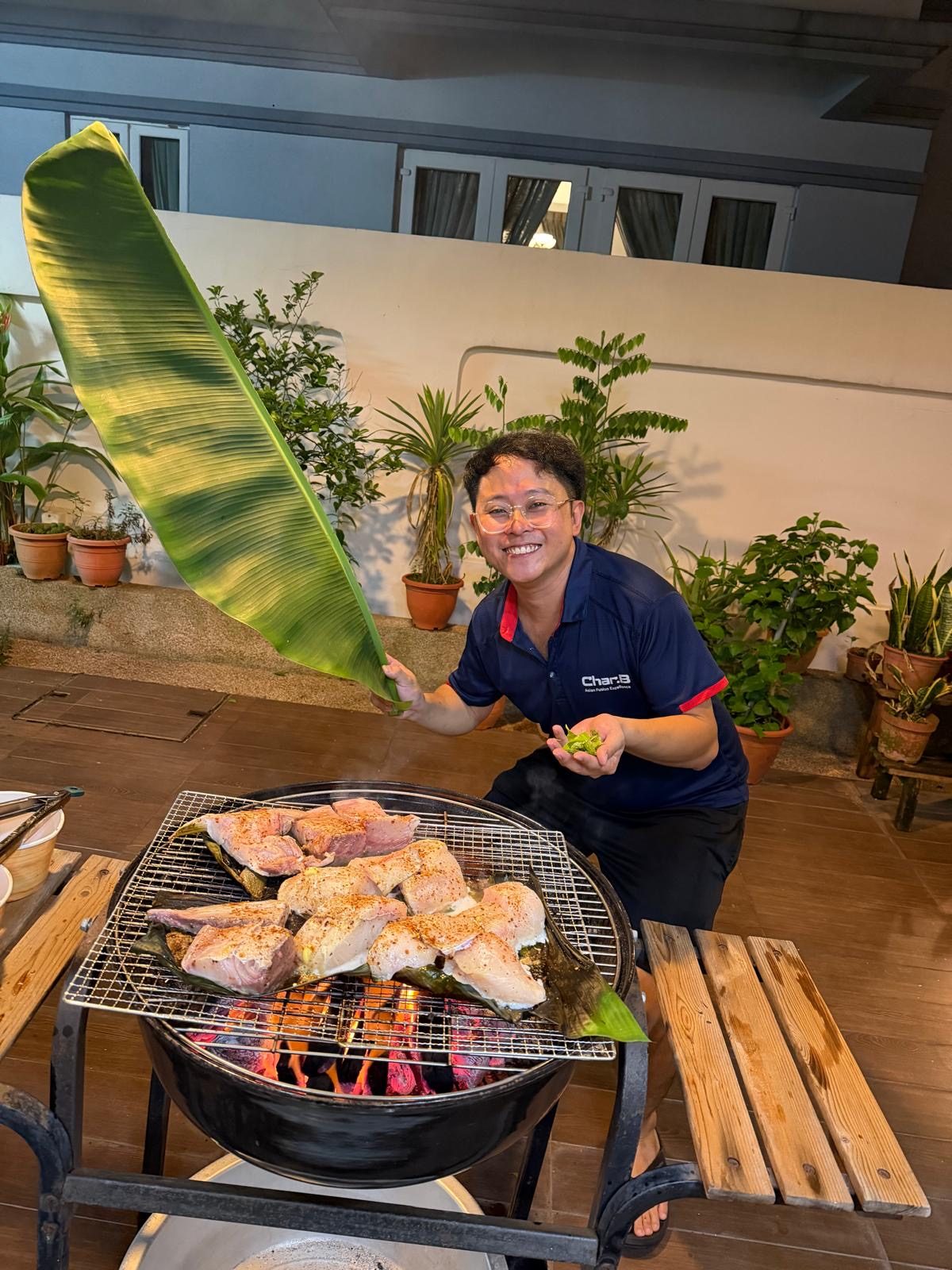 CharB chef grilling fish on banana leaf over charcoal at a home gathering